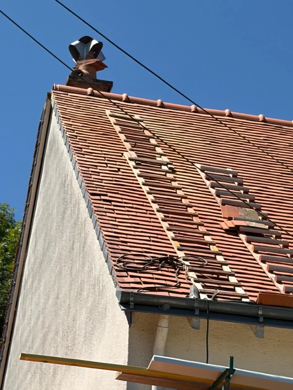 Toiture en tuiles partiellement découverte, liteaux visibles, pendant une reprise de couverture